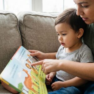 Parent reading a bilingual picture book to a child on a sofa.

